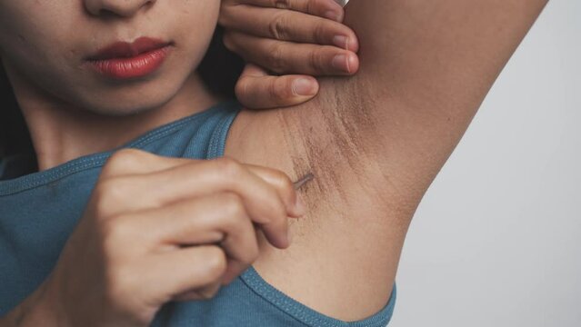 Use tweezers to pull armpit hairs. Young confident asian chinese female armpit with blue tank top isolated background.