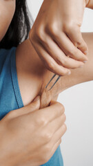 Use tweezers to pull armpit hairs. Young confident asian chinese female armpit with blue tank top isolated background.