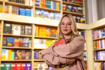 Pretty blonde woman standing with books in library