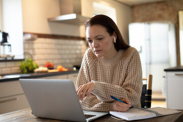 Young woman working on her laptop in the kitchen