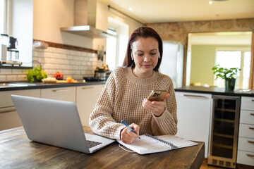 Young adult woman using her laptop and phone at home