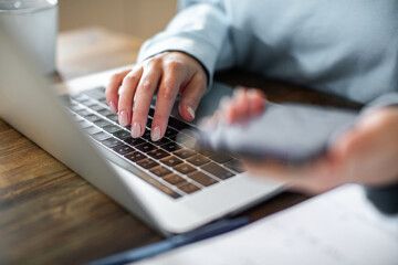 Young adult woman using a banking app on her phone while working from home