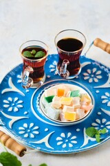 Oriental sweets, cubes of Turkish delight with different flavors in a white bowl on a round blue tray on a light concrete background.