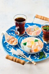 Oriental sweets, cubes of Turkish delight with different flavors in a white bowl on a round blue tray on a light concrete background.