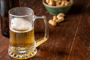 Glass of freshly poured beer on a wooden table next to some nuts as a snack