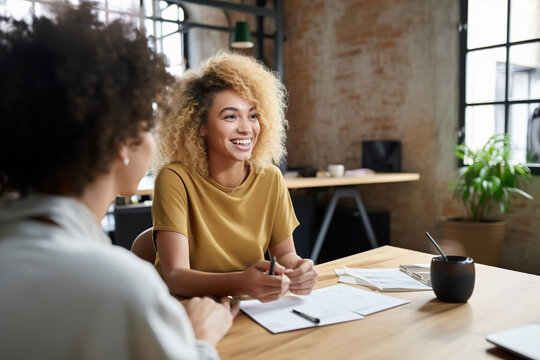 Generative AI illustration of positive young female colleagues with Afro hair smiling and discussing business strategy while sitting at wooden table in modern workspace together