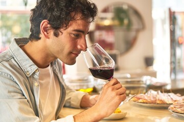 Young man enjoys wine tasting at bar counter.