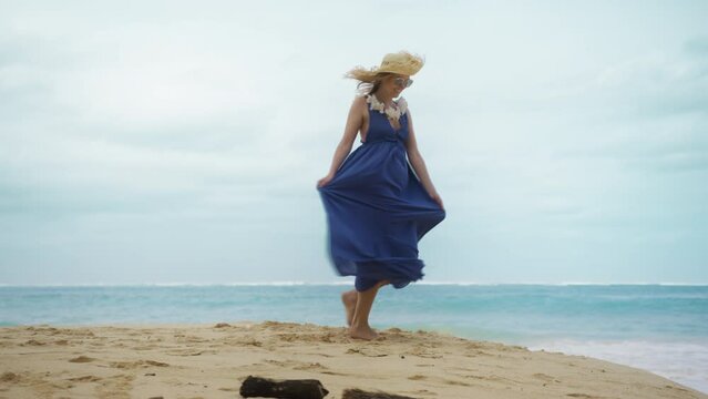 Young woman in beach boho maxi dress and big straw hat dancing and spinning around on sandy beach t teal blue ocean and enjoys the view of sea on Hawaiian island of Oahu, shot on RED 4K tourism USA