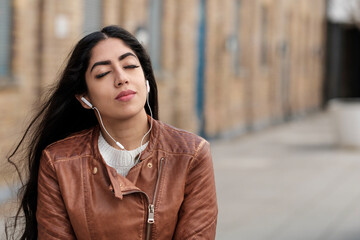 Relaxed young indian woman listening to music outdoors.