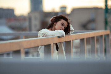 Thoughtful dreamy young brunette leaning on metal railing outdoors