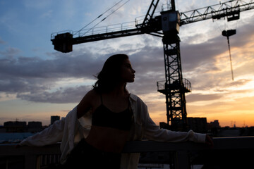 Thoughtful young girl standing on background of construction crane at dusk
