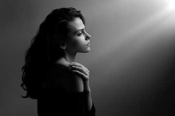 Sad young brunette standing in dark room lighted by sunbeams