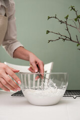 Woman hands are mixing cream for cake on the white table in green background.