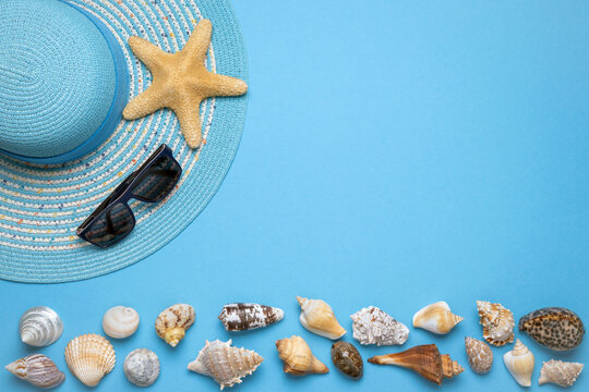 Summer and vacation flat lay with a beauty blue striped woman straw hat, sun glasses, a big star fish and various seashells at the lower edge of the picture on blue background.
