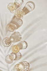 Summer party drinks flat lay, wine glasses with white sparkling wine and palm leaf shadow on light table. Minimal pattern with beautiful wine glasses, above view still life, beige golden neutral color