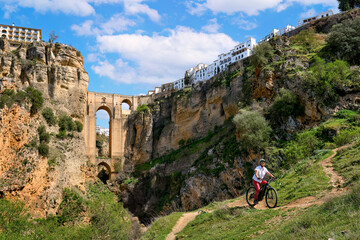 Fototapeta na wymiar nice, active senior woman riding her electric mountain bike below the famous New Bridge of Ronda, Andalusia, Spain