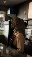 female barista wearing hijab waiting for customers behind coffee shop bar 