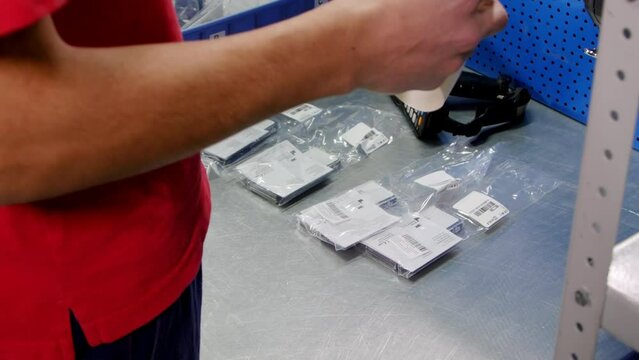 Male warehouse worker in work uniform removes stickers from paper and sticks on consumer goods at workplace. Employee sticks label on each product