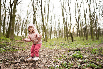 Baby girl playing with sticks in spring forest.