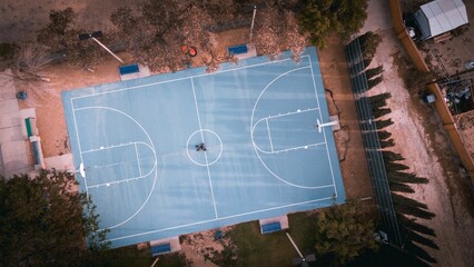 Aerial top view over a basketball court surrounded by trees on a street in a city © Eric Pargas/Wirestock Creators