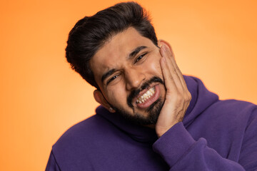 Indian bearded man touching sore cheek suffering from toothache cavities, gingivitis waiting for...