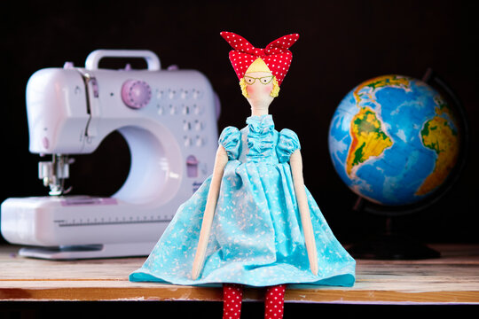 Handmade doll girl tilda near the globe and sewing machine on dark background. Holidays decoration. Interior fairy dolls