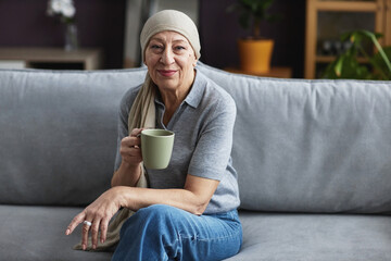 Portrait of mature bald woman smiling at camera relaxing at home with cup of coffee, copy space