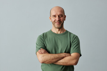 Minimal waist up portrait of mature bald man smiling at camera while standing confidently with arms crossed, copy space