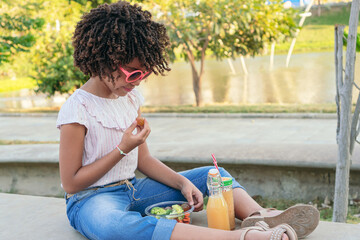 girl eating vegetables while sitting in the park in summertime