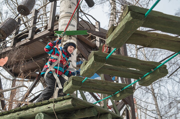 A cute little boy in a hard hat climbs in an adventure park, passing an obstacle course. high rope park