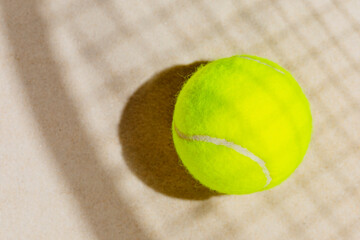 Tennis yellow ball on the sand beach with racket shadow. Tennis competitions, healthy sport and outdoor activities concept. Flat lay