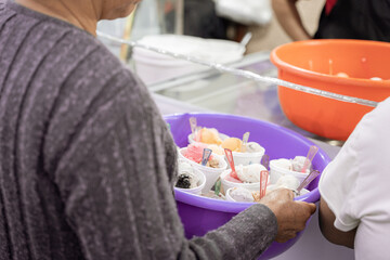An adult Hispanic woman is holding a nest full of prepared ice creams to take away