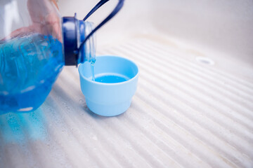 A young woman is filling a cup with blue liquid detergent on a traditional sink