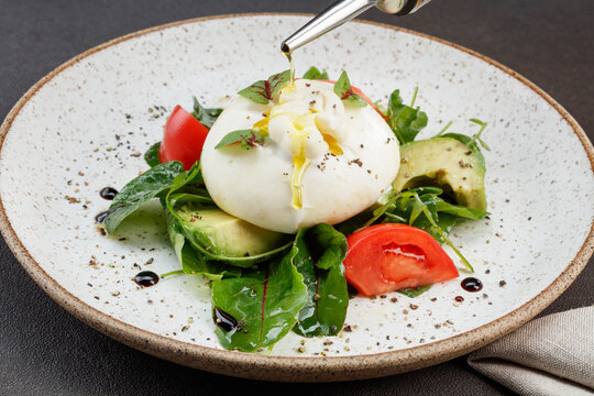 Salad with farmer's burrata, ripe Brazilian avocado, juicy tomatoes, homemade balsamic cream, drizzled with olive oil. Shallow depth of field