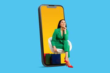 Mobile shopping application. Happy lady sitting in big cellphone screen with shopper bags over blue studio background