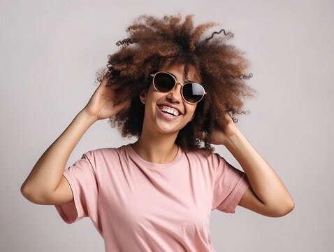 Junge selbstbewusste Frau mit Afro Haaren tanzt und lächelt glücklich in modischem T-Shirt und Sonnenbrille auf weißem Hintergrund, generative AI.