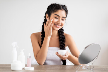 Obraz na płótnie Canvas Skin Care. Smiling Beautiful Indian Woman Applying Moisturising Face Cream At Home