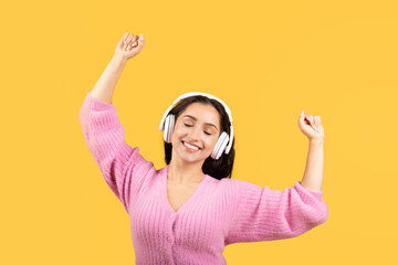 Obraz na płótnie Canvas Cheerful millennial middle eastern lady in wireless earphone has fun, dancing, enjoy music