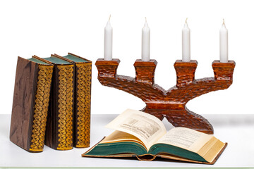 Ancient books and below an open book in front of an antique wooden candlestick on a light table isolated on a white background.