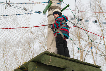 A cute little boy in a hard hat climbs in an adventure park, passing an obstacle course. high rope park - 593659204