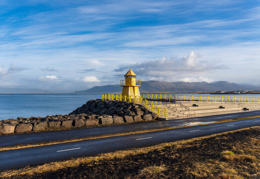 Reykjavik, Iceland: H&ouml;f&eth;i lighthouse (Hofdi Lighthouse) and viewing platform on S&aelig;braut Road looking out over Faxafl&oacute;i Bay and Mt. Esja. Yellow lighthouse on Faxafloi Bay. 