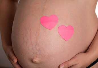 Big belly of a pregnant girl with two pink hearts. The concept of the birth of a child, love and motherhood. Copy space for text