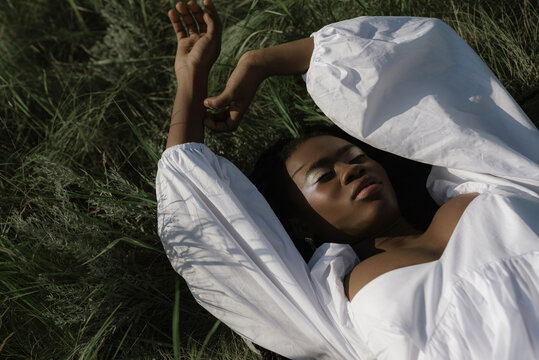 Woman lying on grassy field in a white dress with hands above