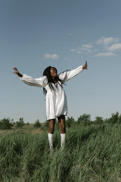 Joyful black woman jumping in field with raised arms