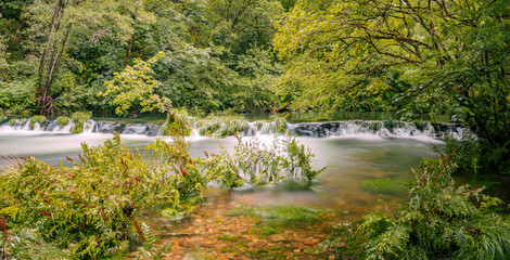 Panoramic landscape of the recreational area of ​​Ponte Segade, La Coruña, with a waterfall on the Sor river, surrounded by green vegetation, leaves and transparent water in summer of 2021 Spain