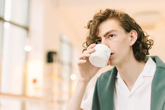Young Man with Long Hair  and Stylish Dress Drinks in Cafe