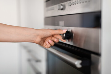 Unrecognizable Female Using Modern Electric Stove In Kitchen, Turning Knob With Hand