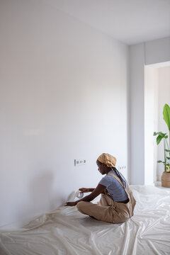 Black woman covering baseboard with painter tape