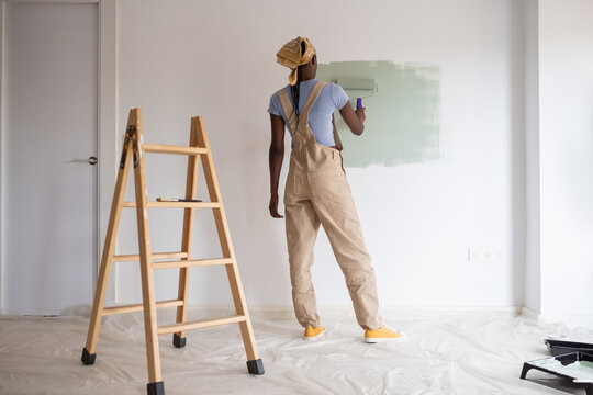Black woman painting wall near door