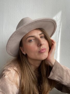UGC . selfie of a woman in a light felt hat on a white wall background
